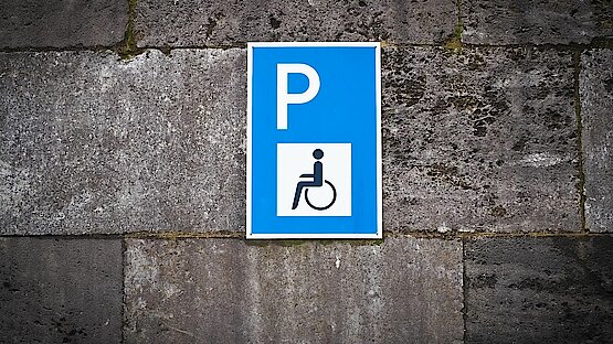 graue Wand mit blau/weiß Parkschild mit Rollstuhl Piktogram