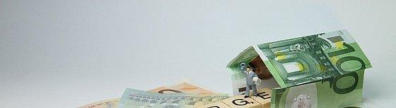 Vorsorge und Rente als Scrabblewörter zusammen gesetzt dazu ein Haus aus 100 Euro scheinen und kleine Figuren ringsrum ein paar Münzen