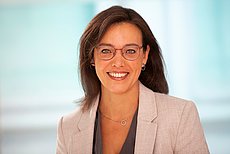 zu sehen ist eine Frau mit Brille, weisser Blazer und lange dunkle Haare